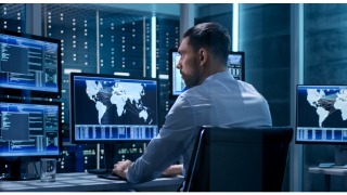 Man sitting in front of multiple monitors with a global map on the screen.