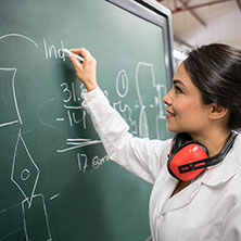 A female engineering student working on a chalk board figuring out a physics equation. - Faculty Innovation Grant Awardees 2021-2022