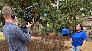 A videographer filming a student speaking on campus.
