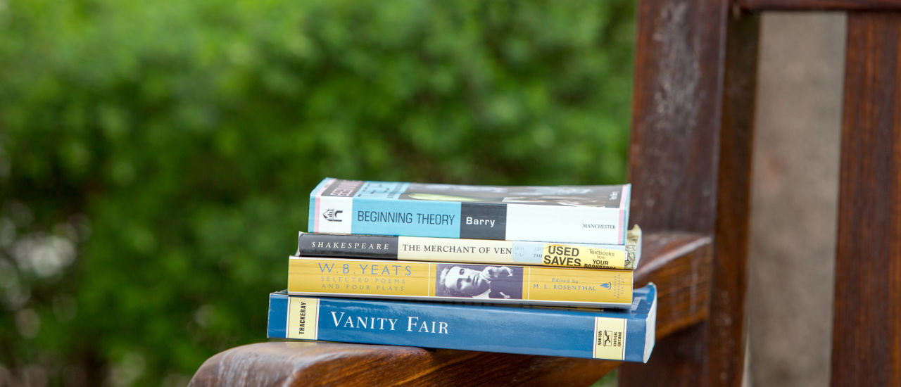 Four paperback books stacked on a bench.
