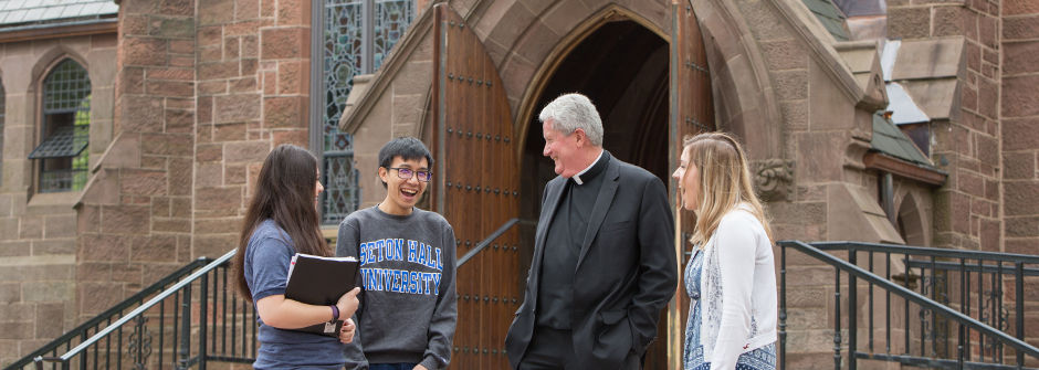 A priest laughing with students outside the Chapel of Immaculate Conception. 