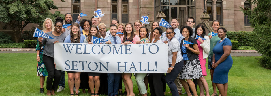 A photo of the admissions counselors team holding a Welcome to Seton Hall sign on the University Green. 