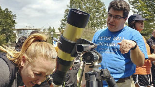 Professor Jose Lopez explaining the science behind the solar eclipse to a student looking through a telescope. 