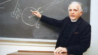 Image of Father Stanley Jaki in front of a blackboard with diagrams related to physics on the board