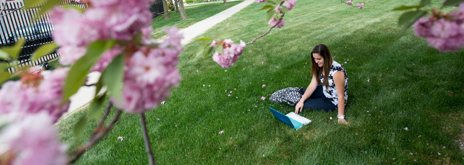 Student on laptop sitting on the grass. 